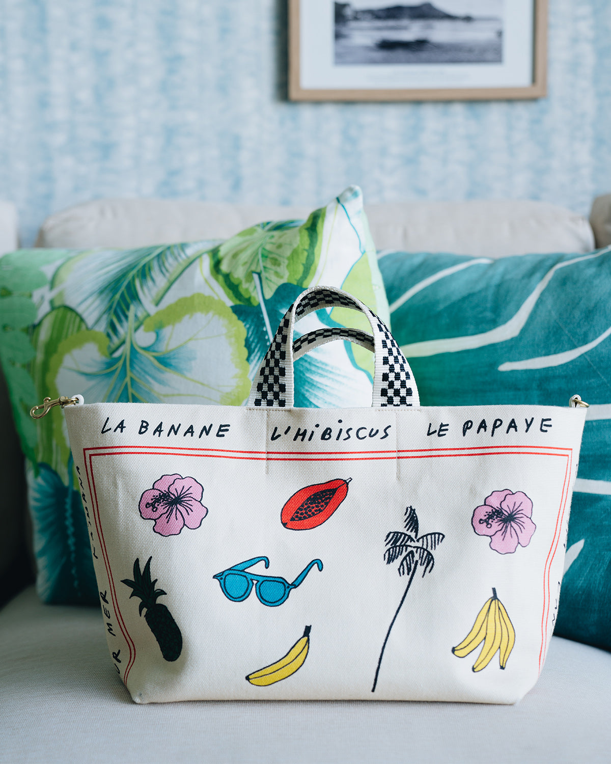 CV x Le Catch Bateau Tote in Natural Paradis Print Sitting on a White Table in Front of Throw Pillows