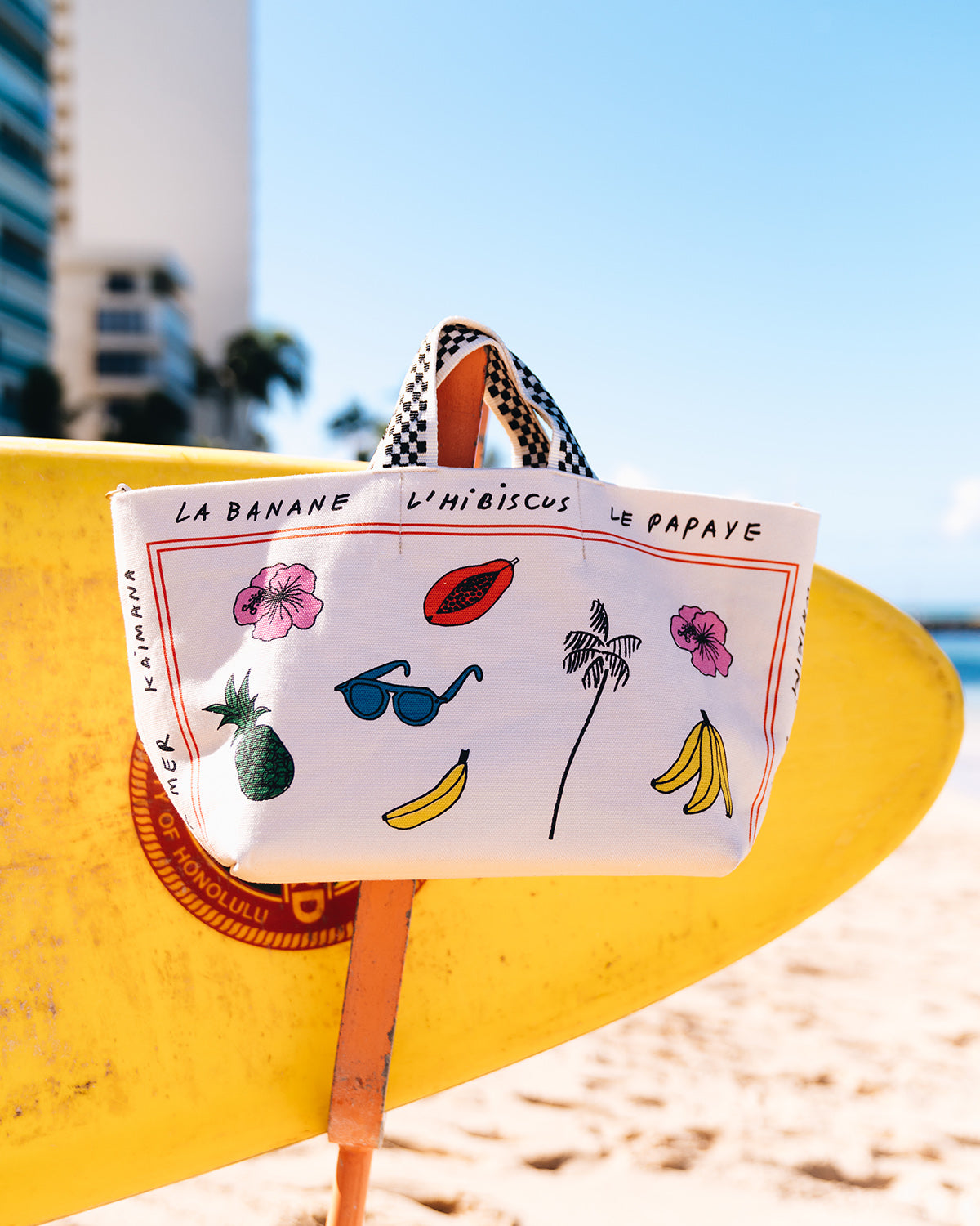 The CV x Le Catch Bateau Tote in Natural Paradis Print Hanging in Front of a Yellow Surfboard