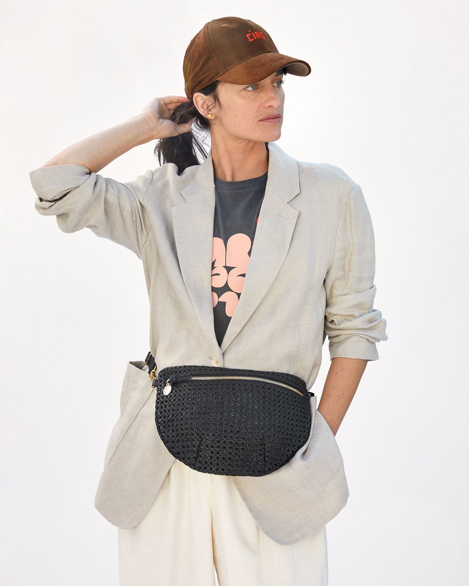 danica wearing the Brown Corduroy Ciao Baseball Hat with cream pants and a light grey blazer with the black rattan grandy fanny around her waist