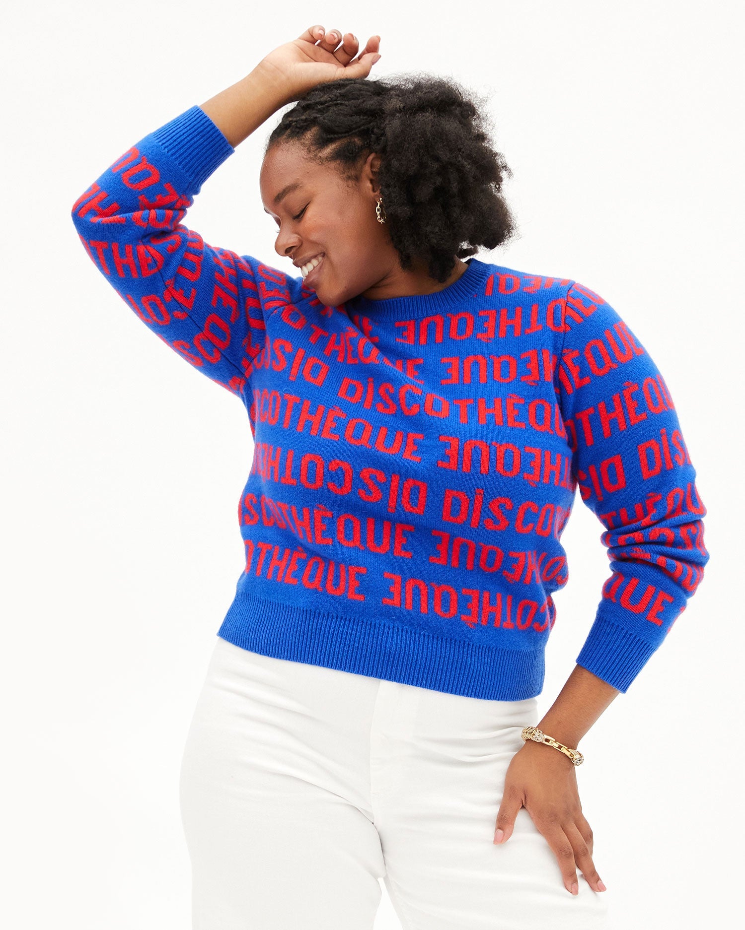 Candace smiling in the Cobalt & Poppy Discotheque Classic Sweater with one of her hands over  her head