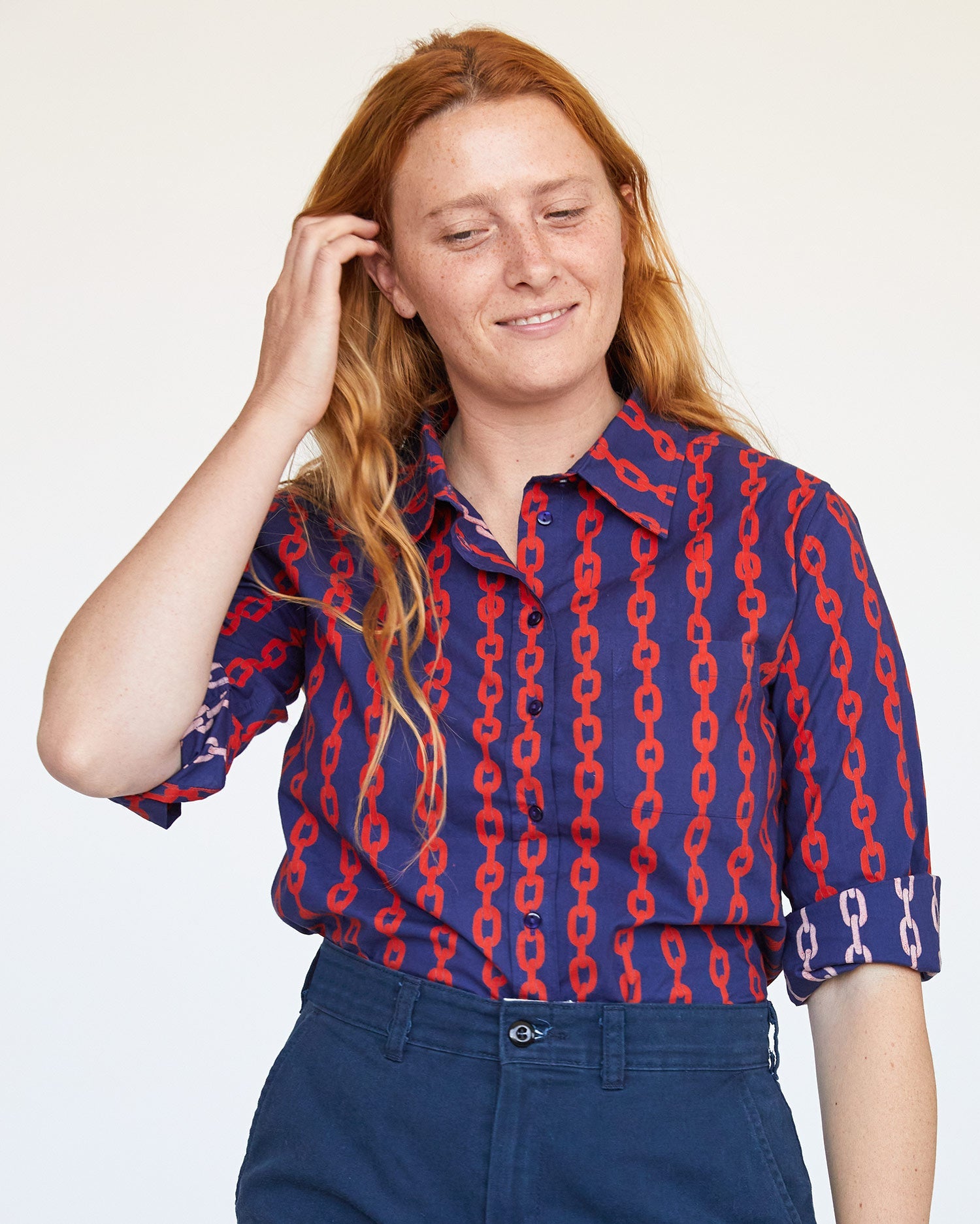 Courtney wearing the Natalie wearing the Navy and Poppy Chains Felix Blouse tucked in to blue slacks, tucking her hair behind her ear