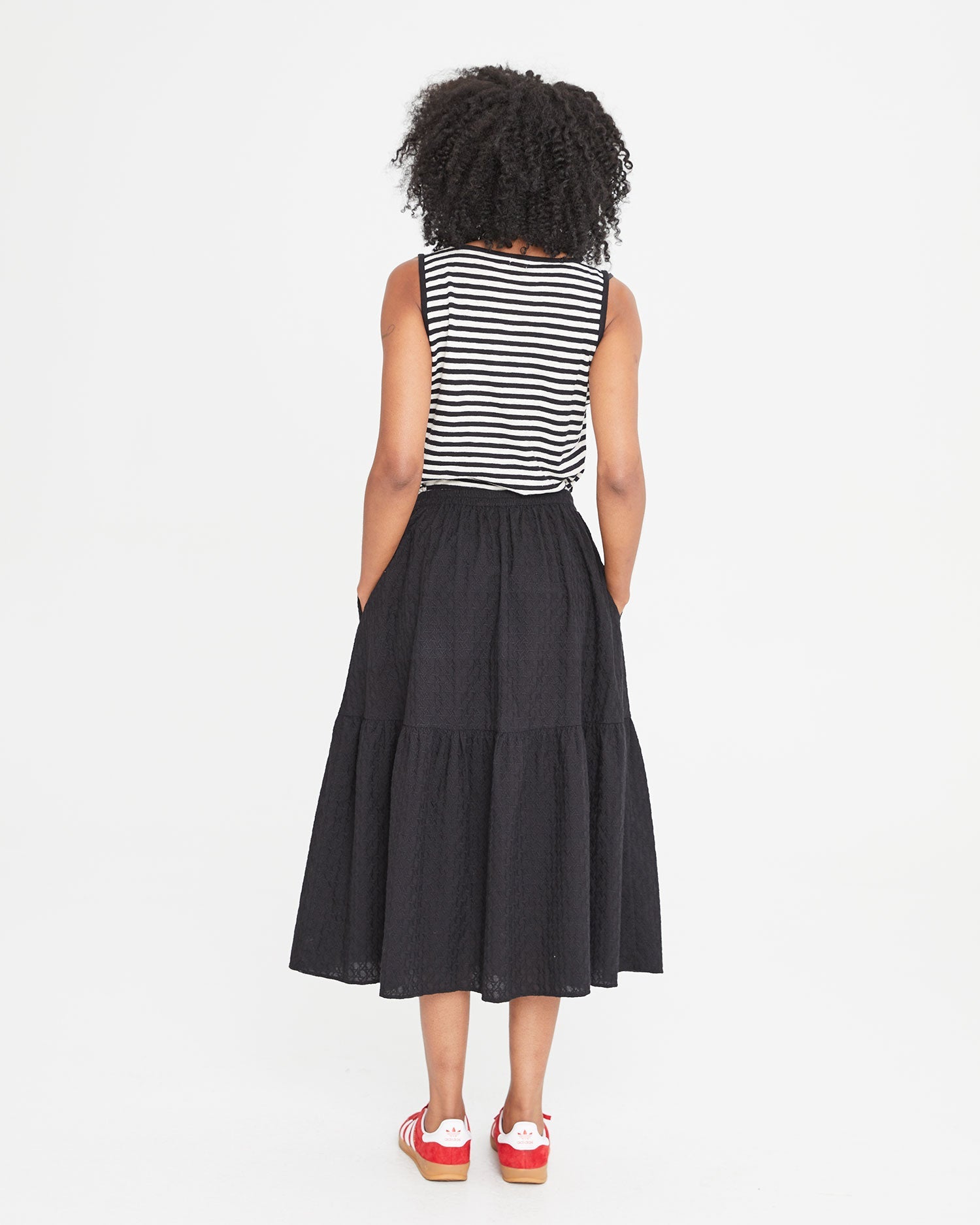 back view of Mecca in the Black Eyelet Rattan Manon Skirt and a black and white striped tank top 