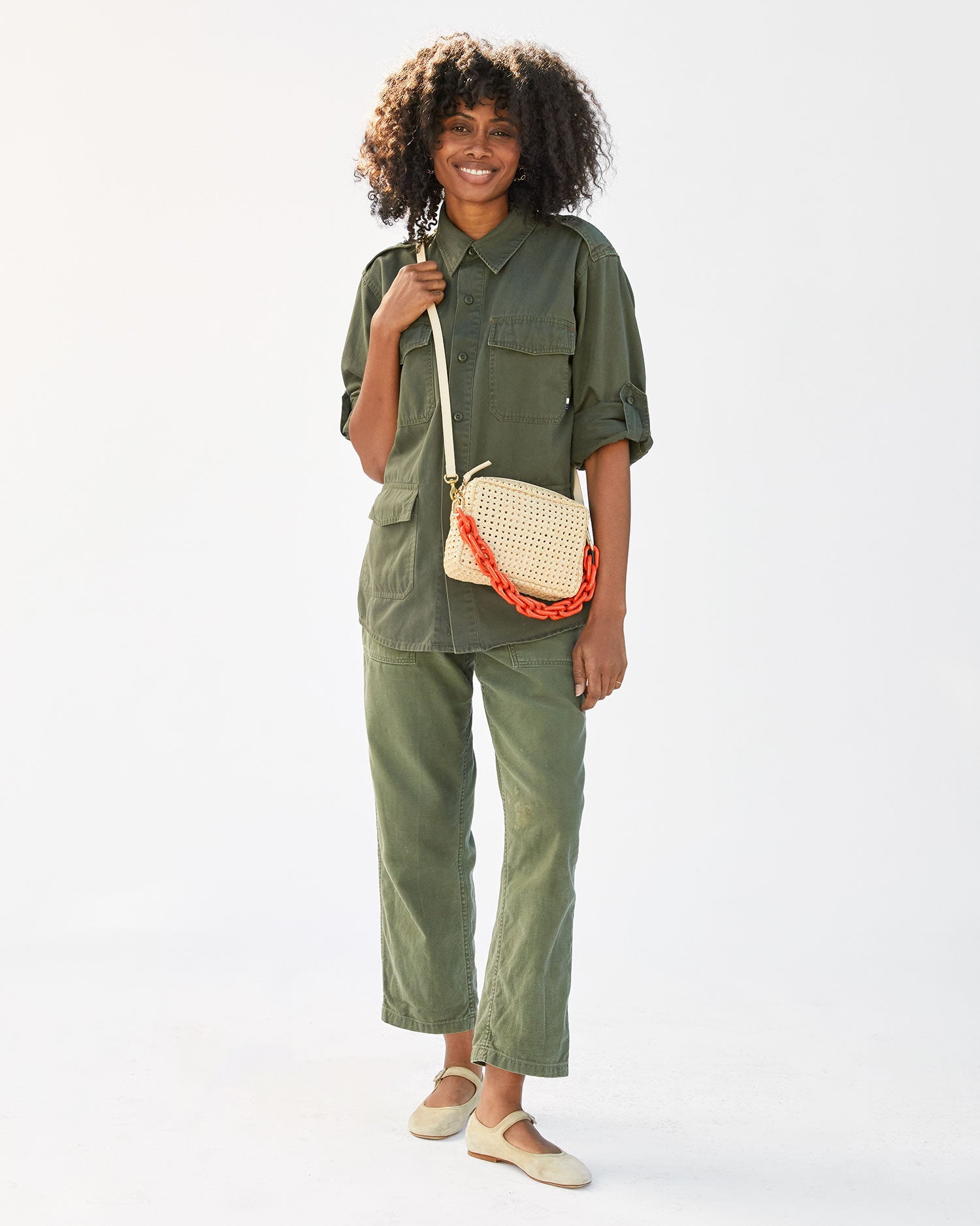 mecca in an army jumpsuit wearing the Cream Rattan Midi Sac with the neon orange short strap