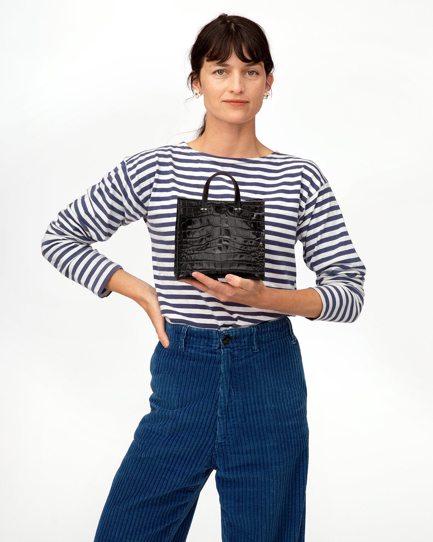 danica wearing a striped shirt and blue cords holding the Black croco Simple Tote Bébé in her right hand in front of her chest