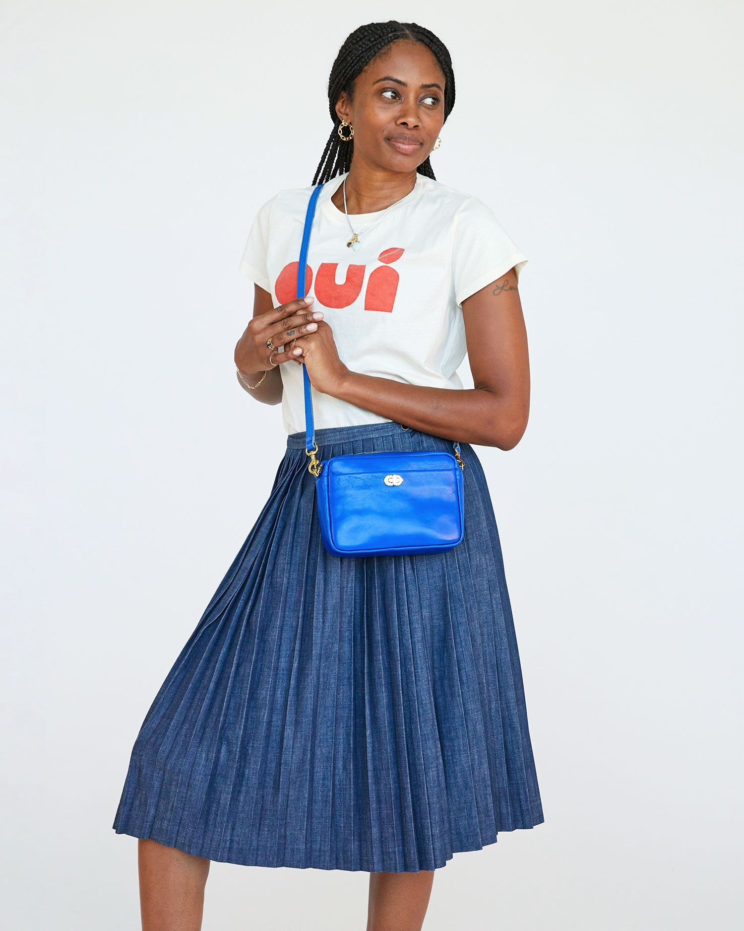 mecca wearing the Electric Blue Turnlock Midi Sac with both of her hands on its crossbody strap. she's looking off to her left