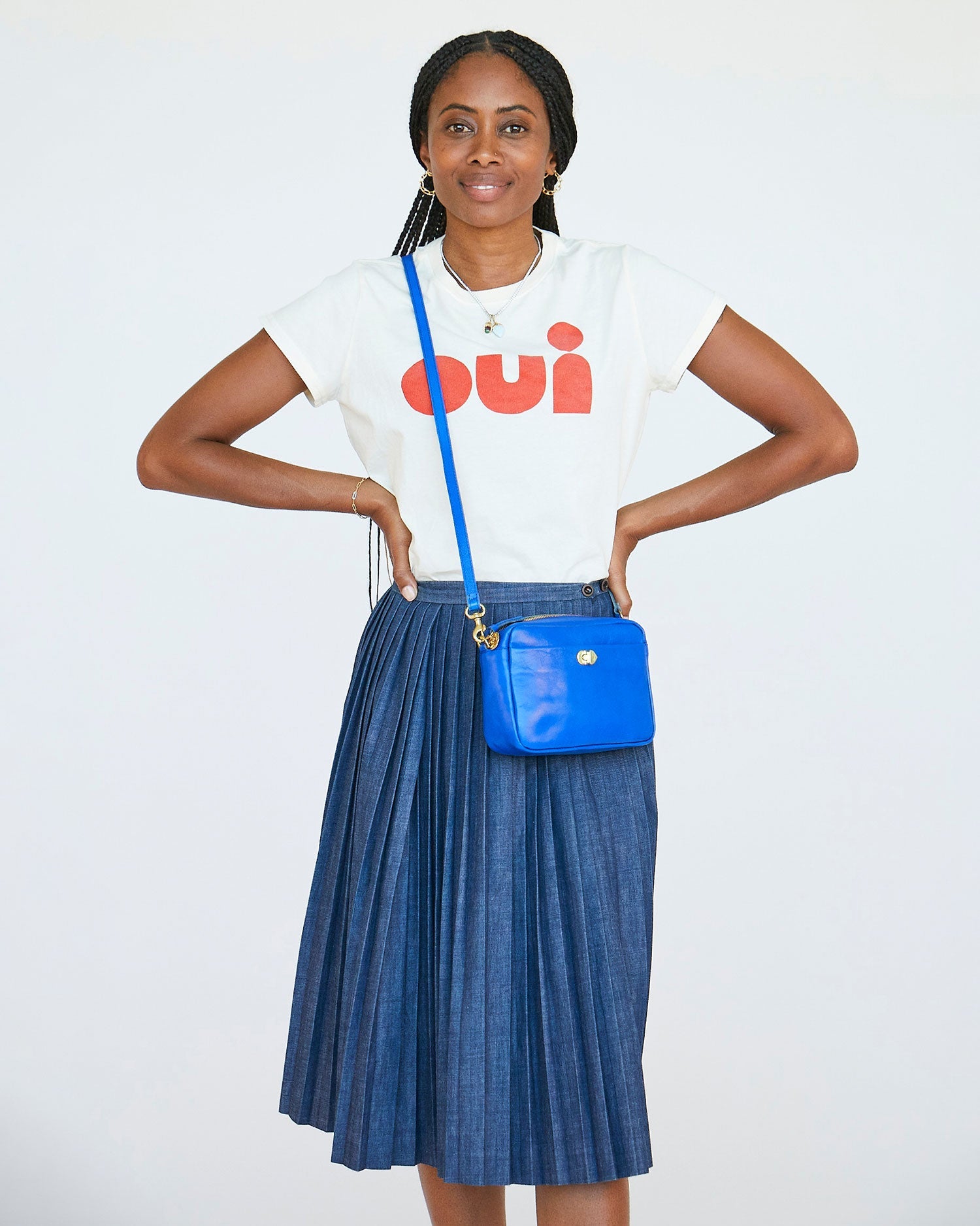 mecca in a pleated blue skirt and a cream oui tshirt wearing the Electric Blue Turnlock Midi Sac crossbody